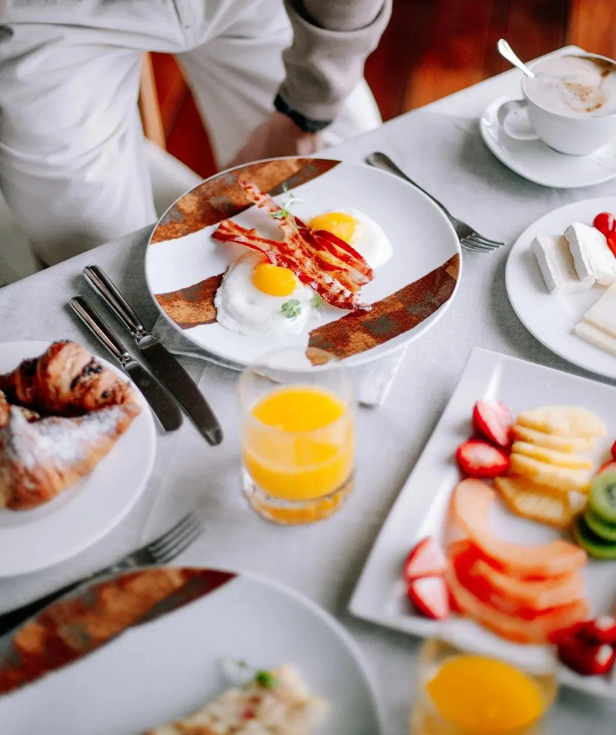 Colazione servita al tavolo: uova e bacon, cornetto, frutta e succo d'arancia