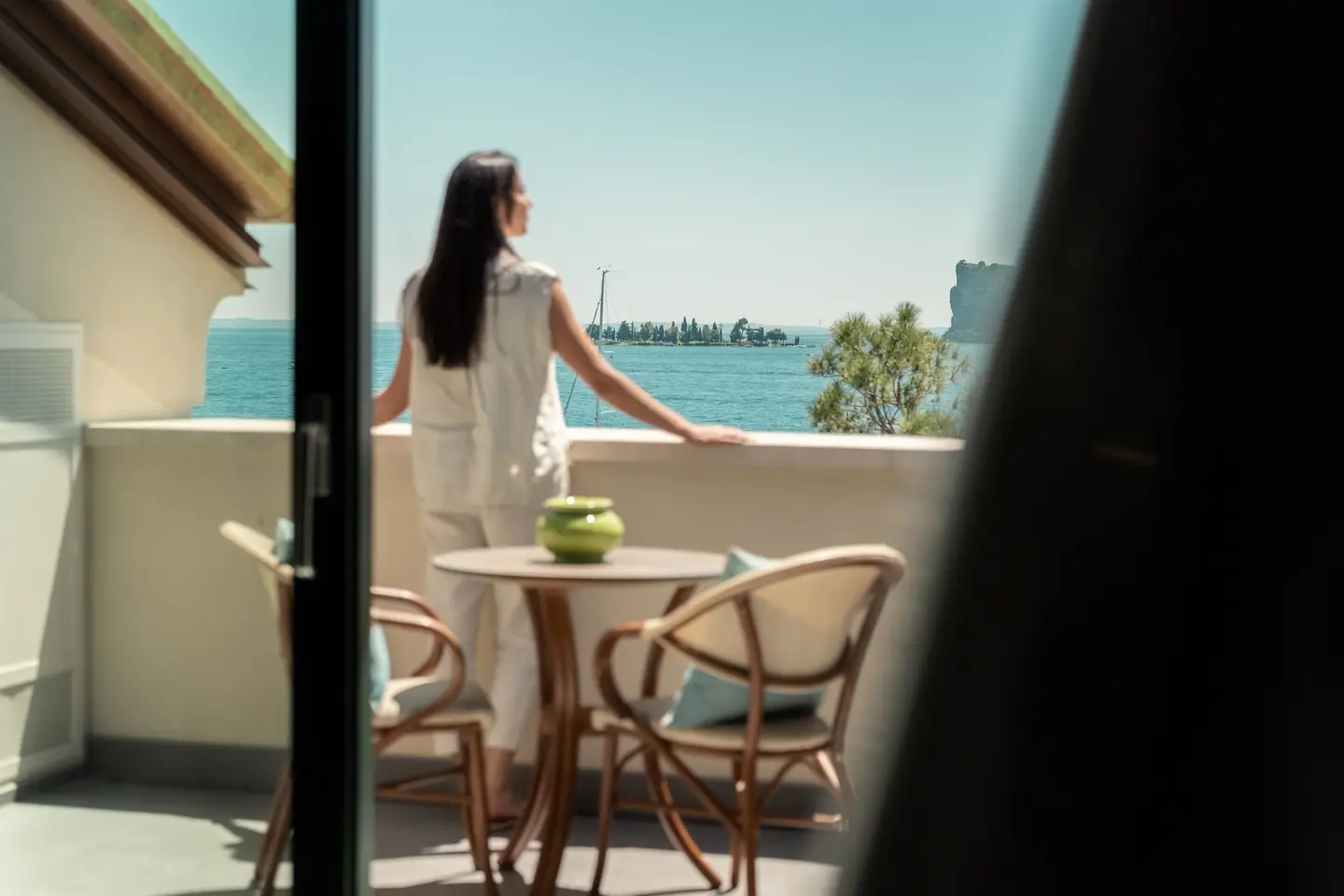A guest on the balcony of a room, with the lake, the Isola del Garda and the Rocca di Manerba