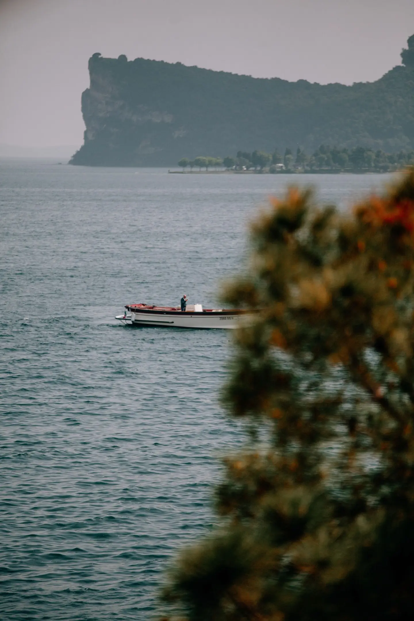 Una barca sul lago davanti alla Rocca di Manerba, vista fra i rami