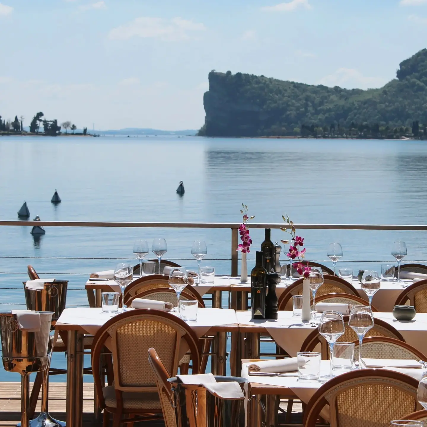 Tavoli apparecchiati sulla terrazza, con le boe sul lago e la Rocca di Manerba