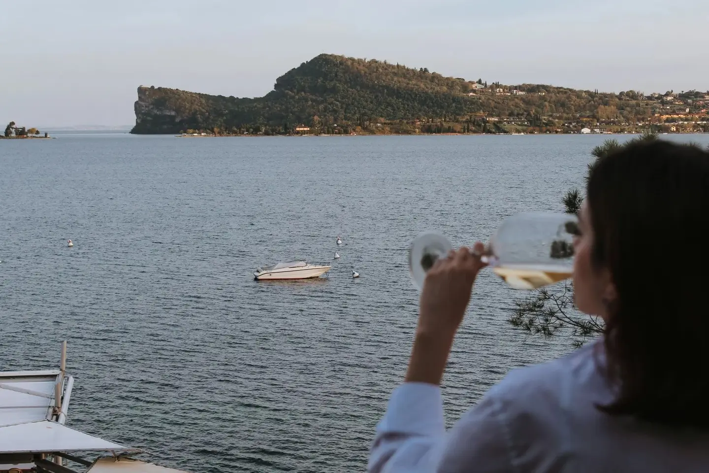 Un'ospite con un calice di vino bianco davanti al lago e alla Rocca di Manerba