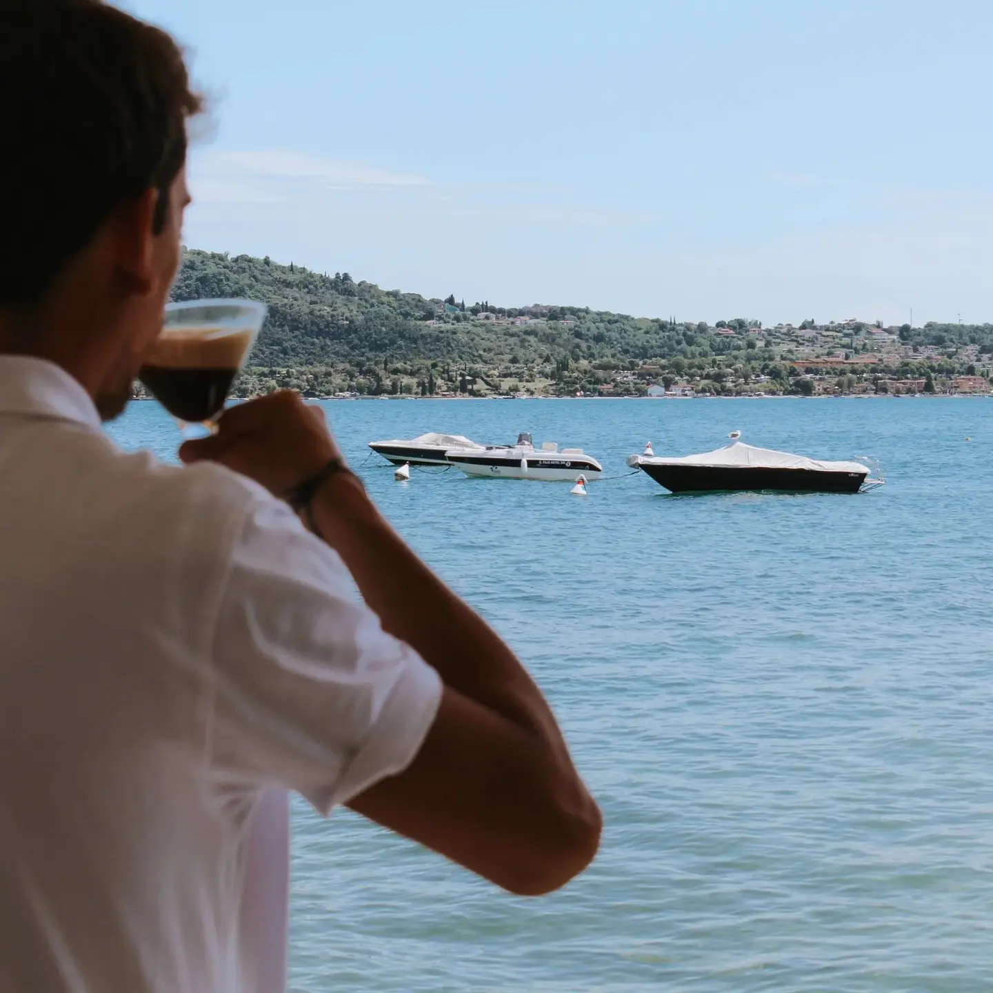 Un ospite beve un caffè guardando i motoscafi sul lago