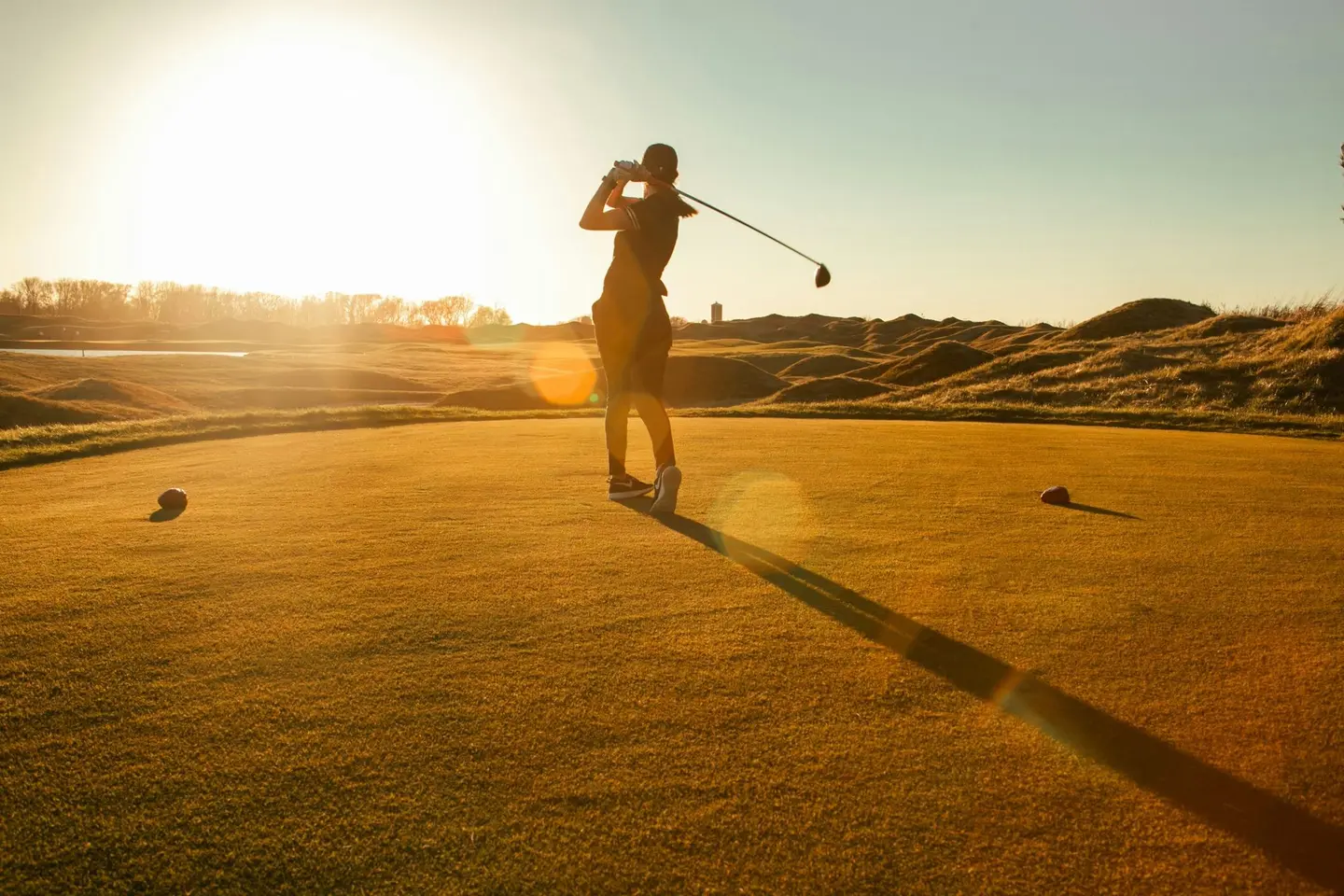Una golfista al tee al tramonto, sul campo da golf