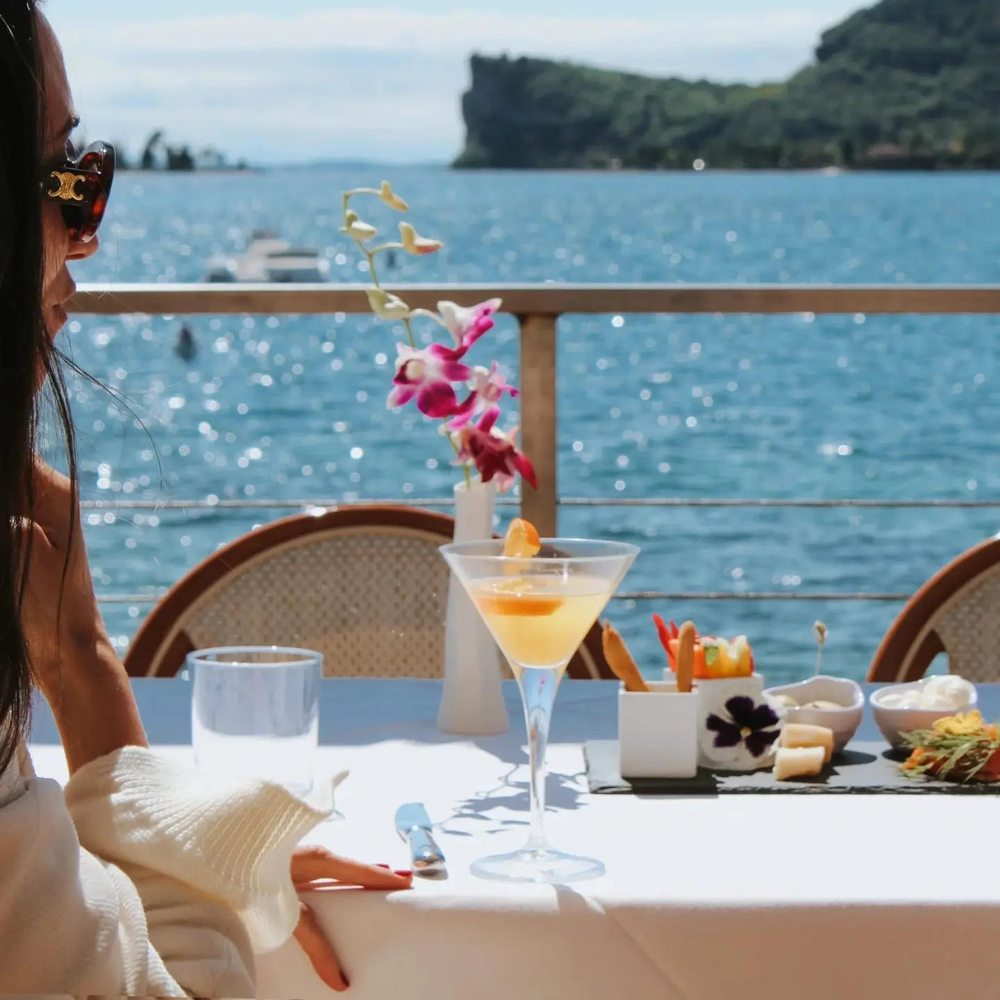 Un'ospite con un cocktail e stuzzichini sulla terrazza, davanti alla Rocca di Manerba