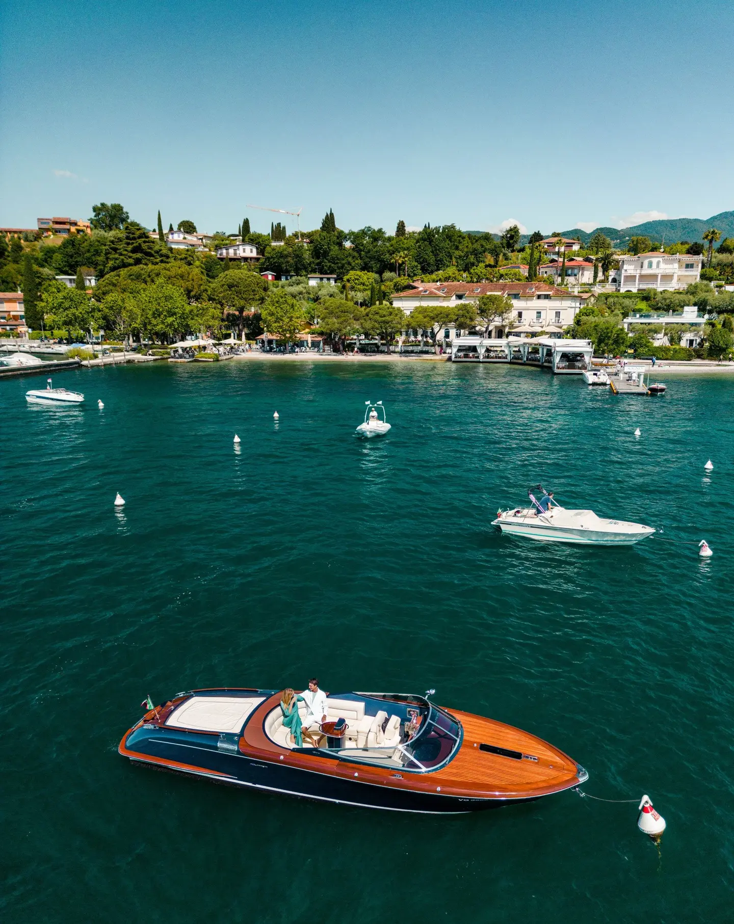 Un motoscafo ormeggiato a una boa sul lago, con l'Hotel Sogno e la riva sullo sfondo