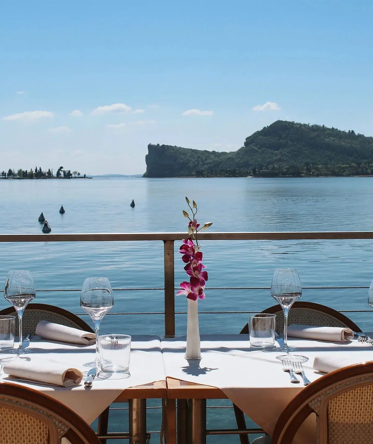 Tavolo apparecchiato con un'orchidea sulla terrazza, davanti alla Rocca di Manerba